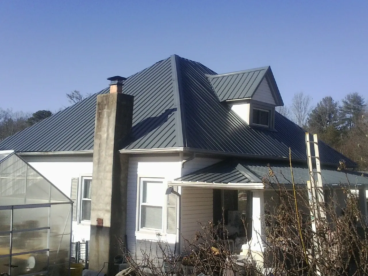 Dark blue standing seam metal roof on a white farmhouse with dormer — Slate & Tile Roof Repair by Roofing Brothers in New Durham