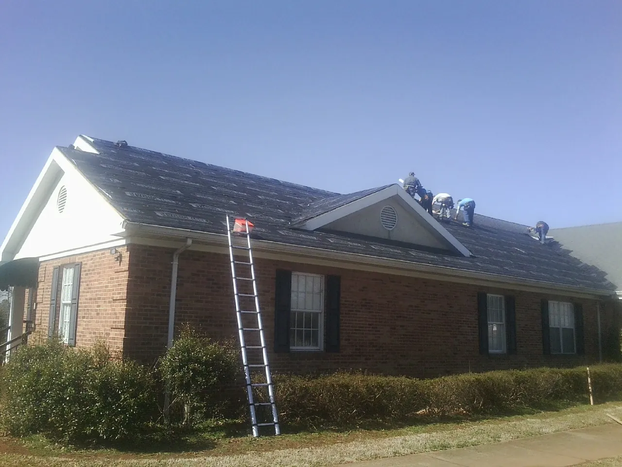 Crew tearing shingles off a brick ranch roof with a ladder set — Emergency Roof Repair work by our crew in New Durham