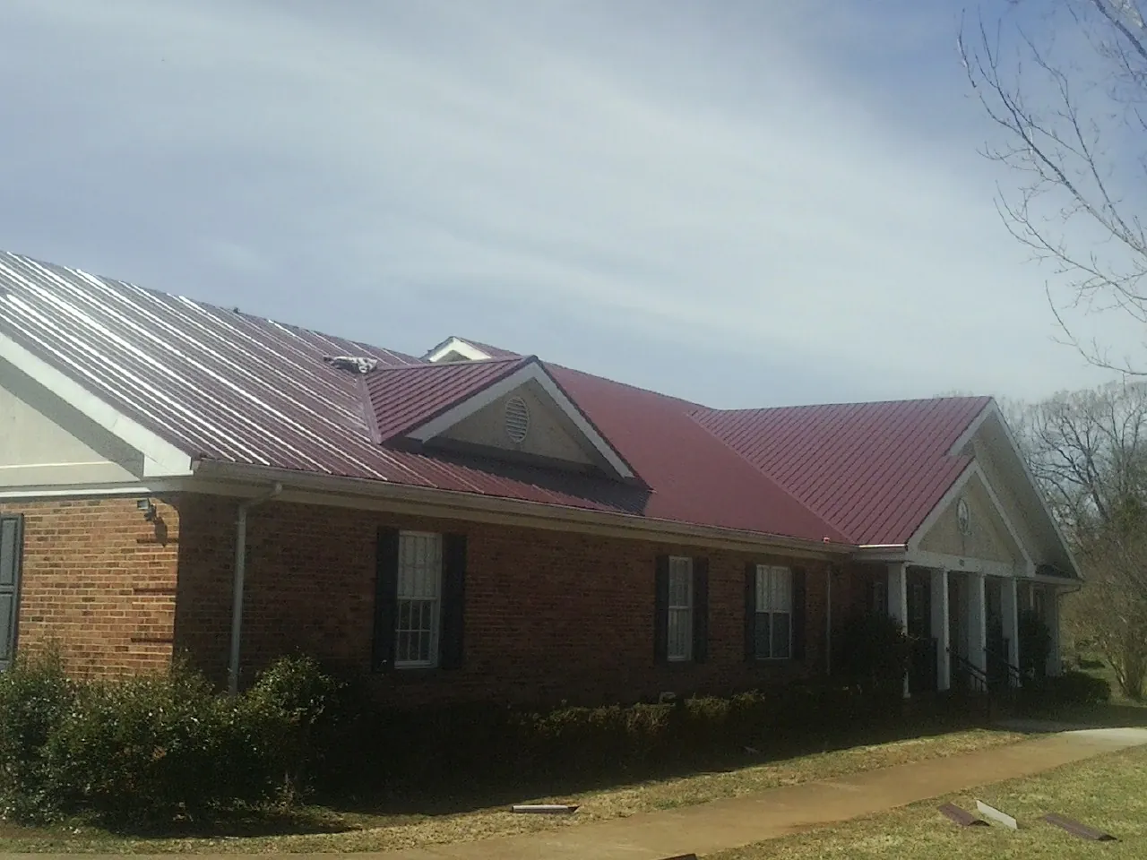 Red metal roof with gabled entries on a long brick building, from a Hail Damage Roof Repair job in New Durham