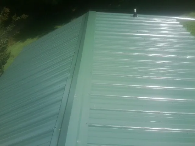 New green metal panels meeting at the ridge of a roof — Flat Roof Repair work by our crew in New Durham