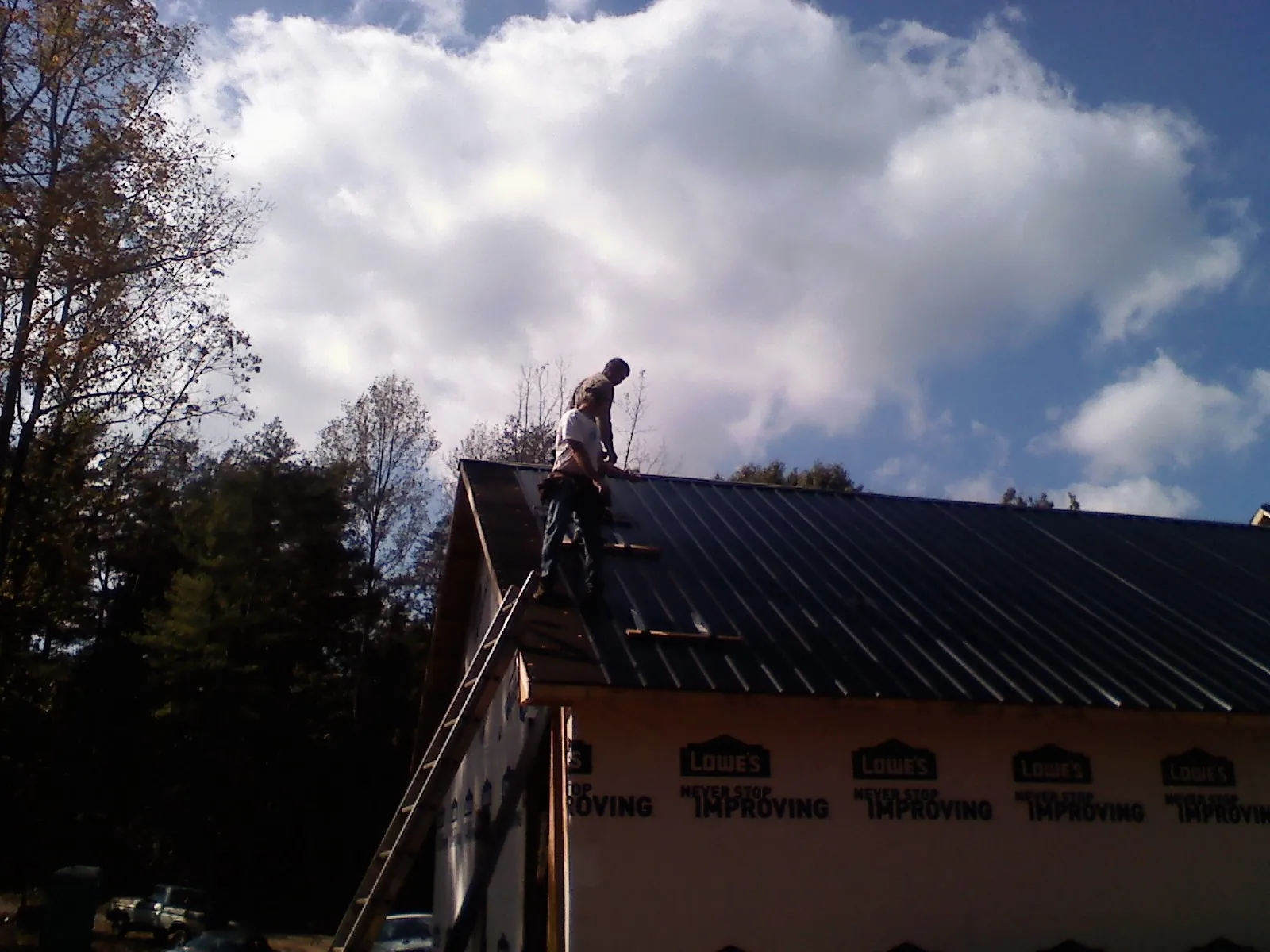 Roofer fastening dark metal panels high against a cloudy sky, from a Roof Inspection job in New Durham
