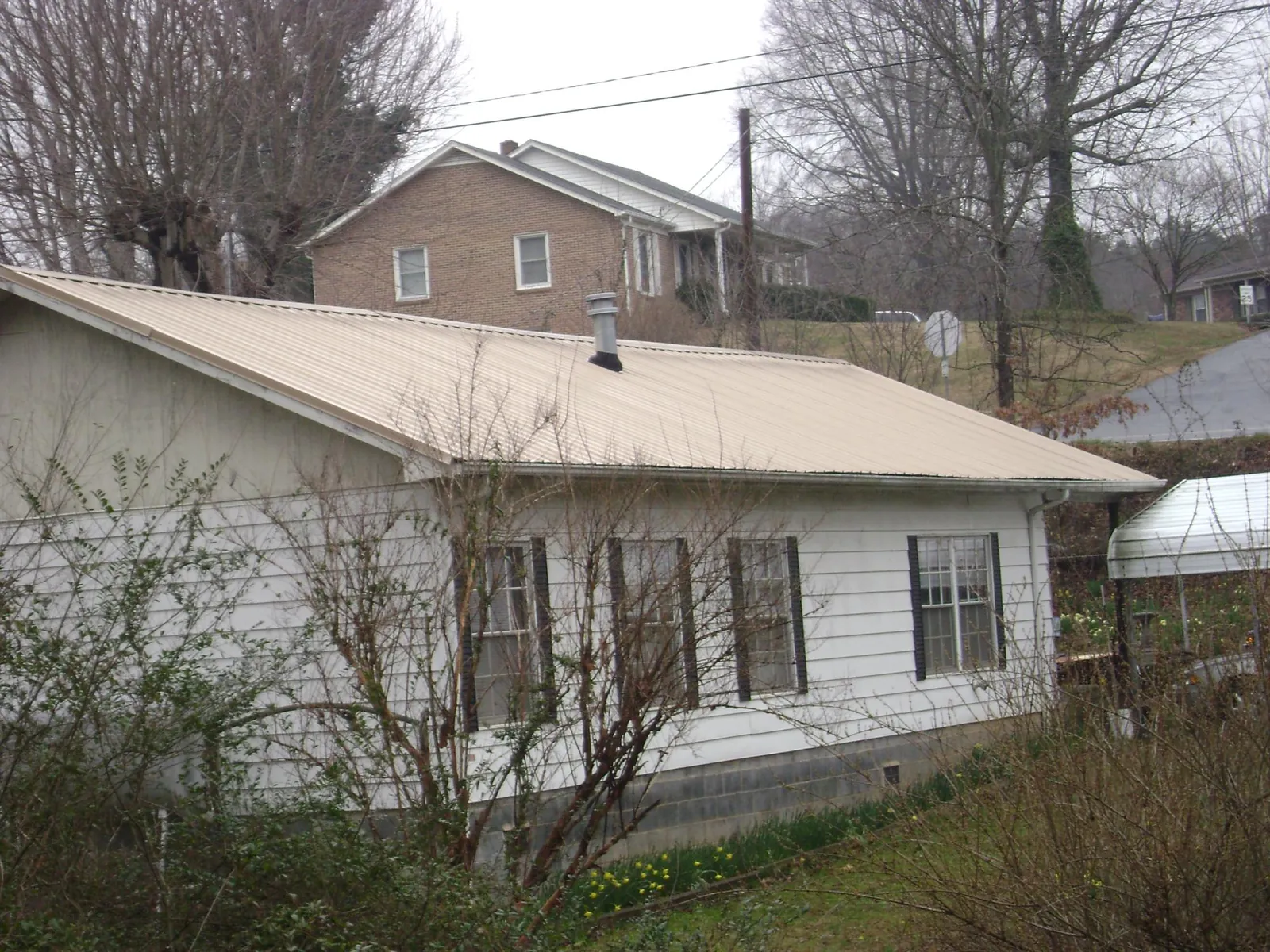 Tan metal roof on a white sided house set into a hillside — Commercial Roofing by Roofing Brothers in New Durham