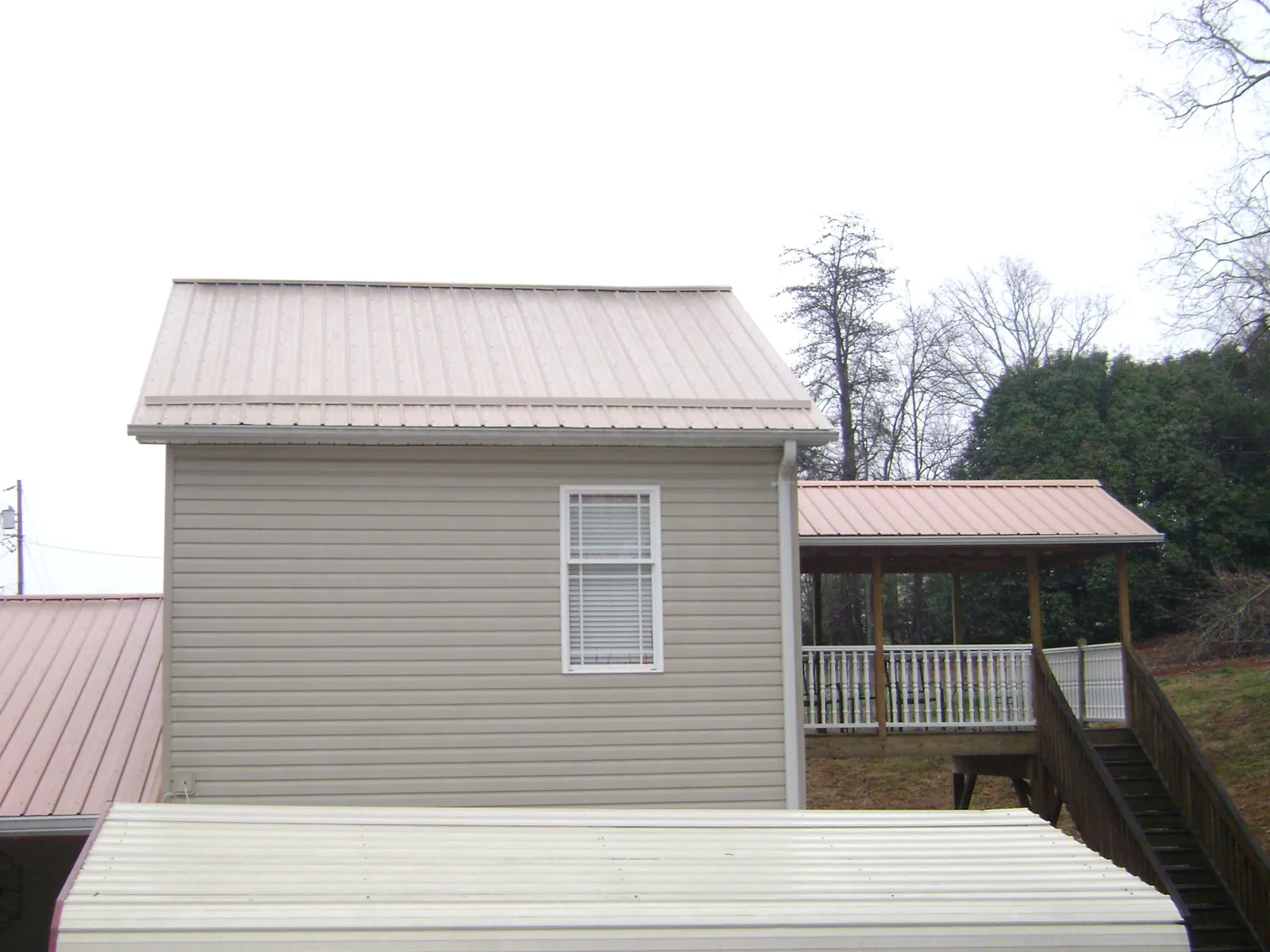 Tan metal roofs on a two story addition and attached porch, from a Roof Replacement job in New Durham